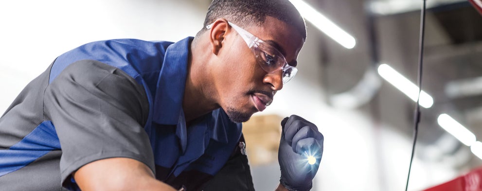 A Subaru technician using flashlight to look into a Subaru engine compartment. | Subaru World of Newton in Newton NJ